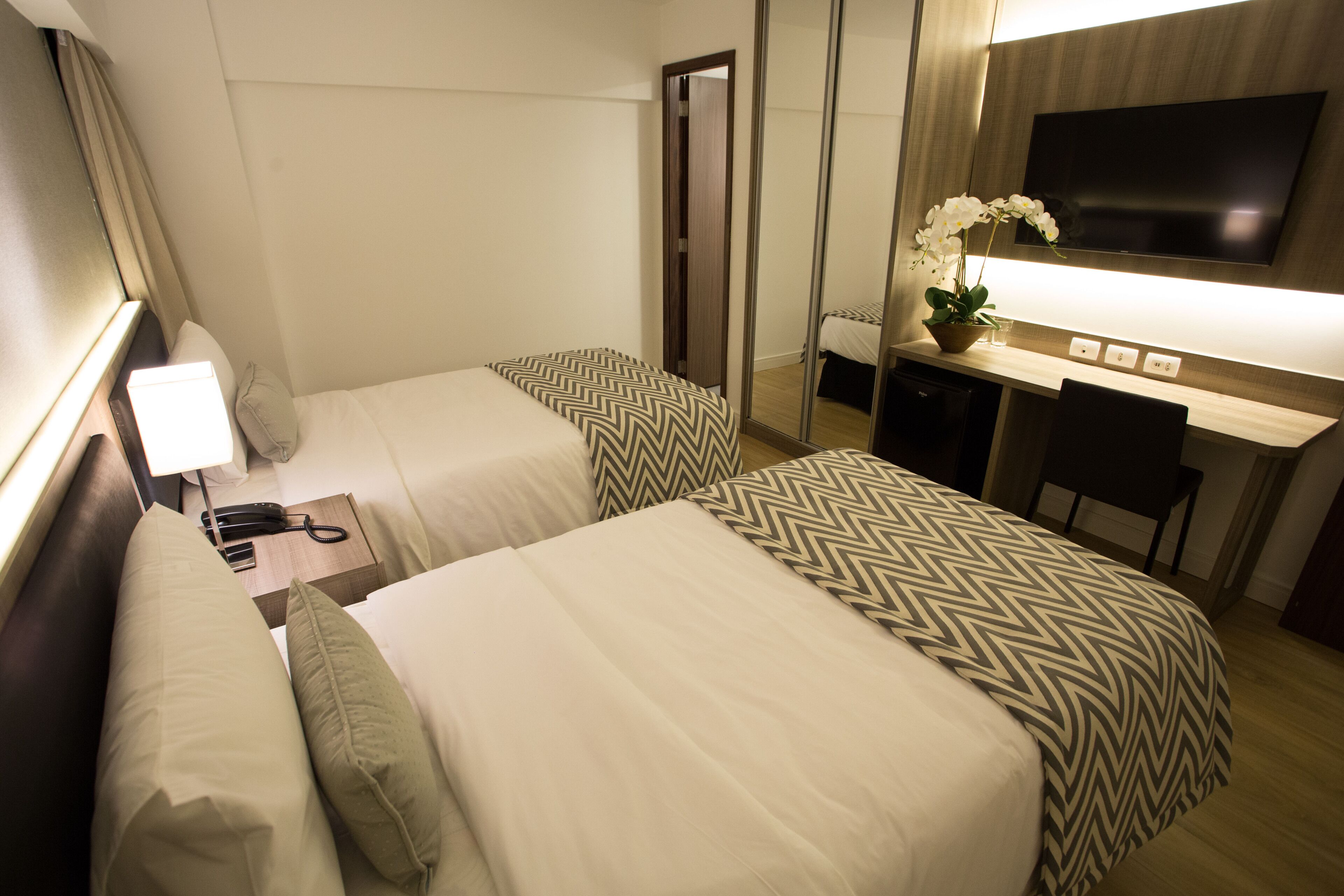 A hotel room with two beds, a desk, a TV, and a mirror.