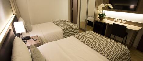 A hotel room with two beds, a desk, a TV, and a mirror.