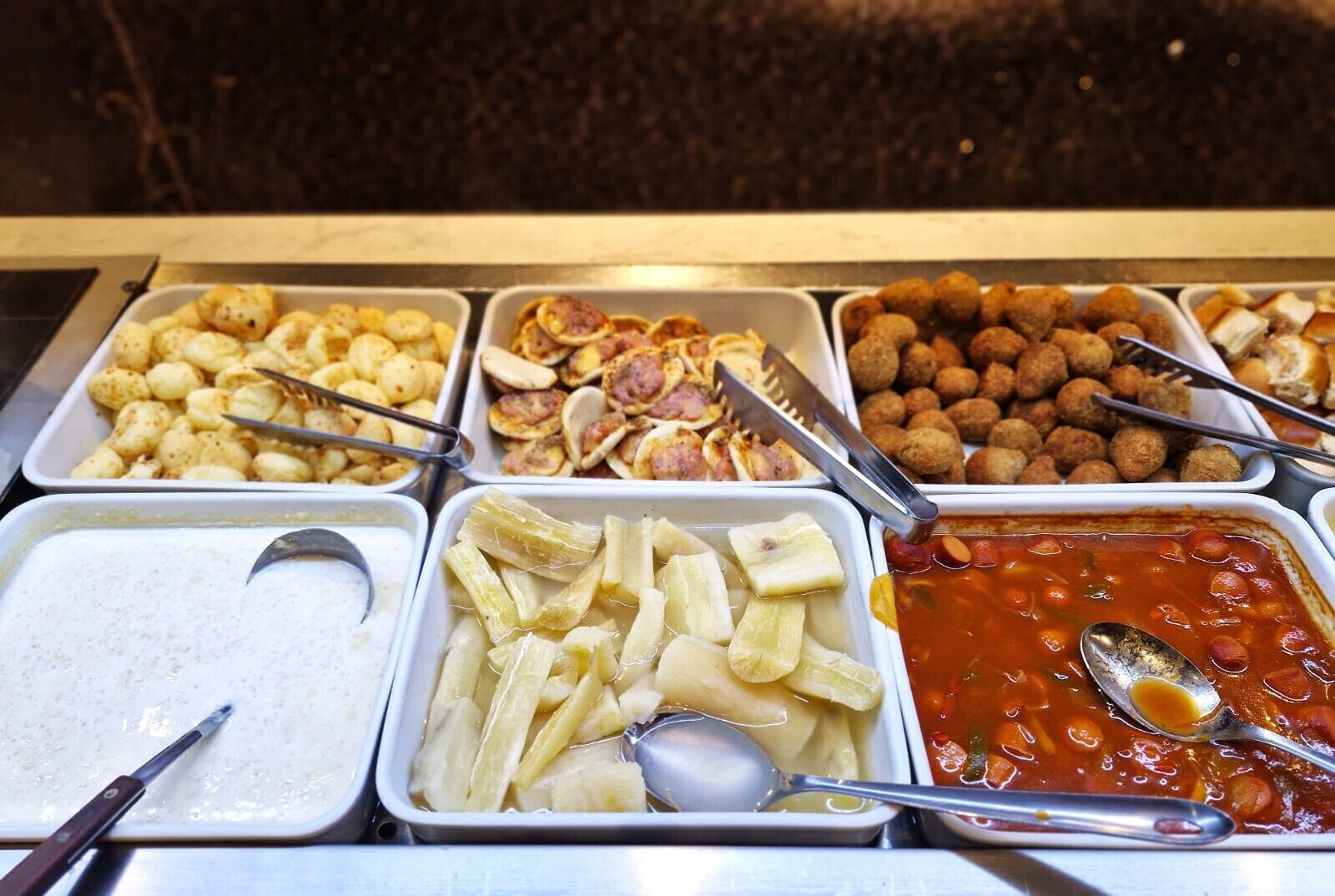 Un bufé con diversas opciones de comida, incluyendo pasta, albóndigas y un plato a base de tomate.