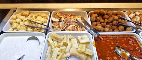 A buffet with various food options including pasta, meatballs, and a tomato-based dish.