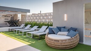Un espace de détente extérieur moderne, doté de chaises longues et d’un canapé en osier, d’un mur en béton et d’une porte en verre.