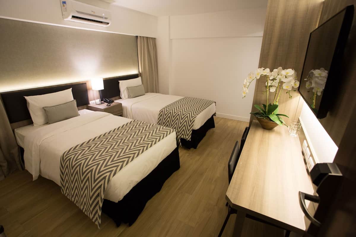Een hotelkamer met twee bedden, een bureau, een stoel, een televisie, een plant en een airconditioning.