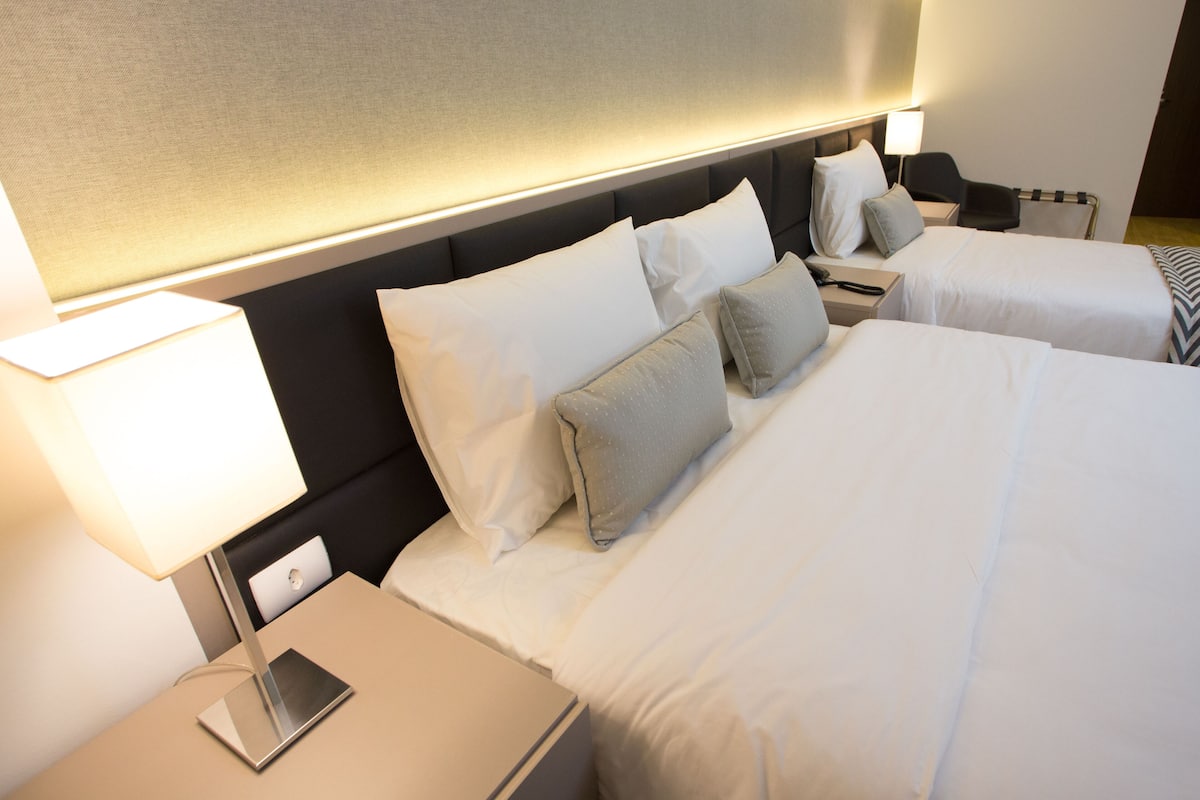 Ein Hotelzimmer mit zwei Betten, einem Nachttisch mit Lampe sowie einem Beistelltischchen mit Telefon.