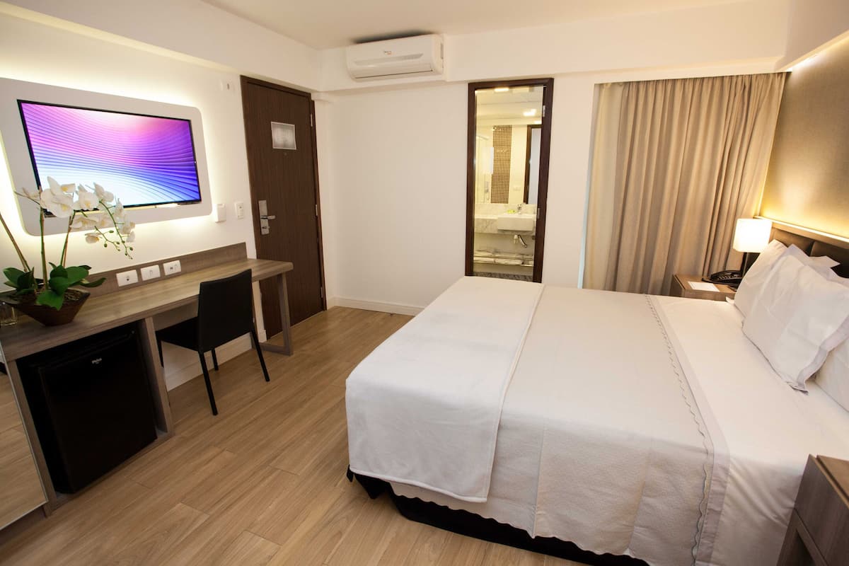 A hotel room with a bed, desk, chair, TV, and a bathroom visible through an open door.