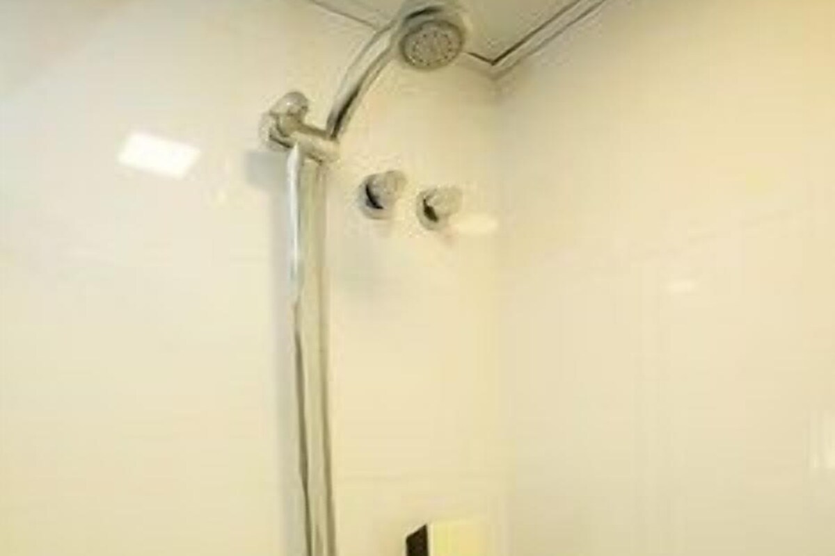 Ducha con cabezal de ducha de mano, panel de control en la pared y llave en el suelo.