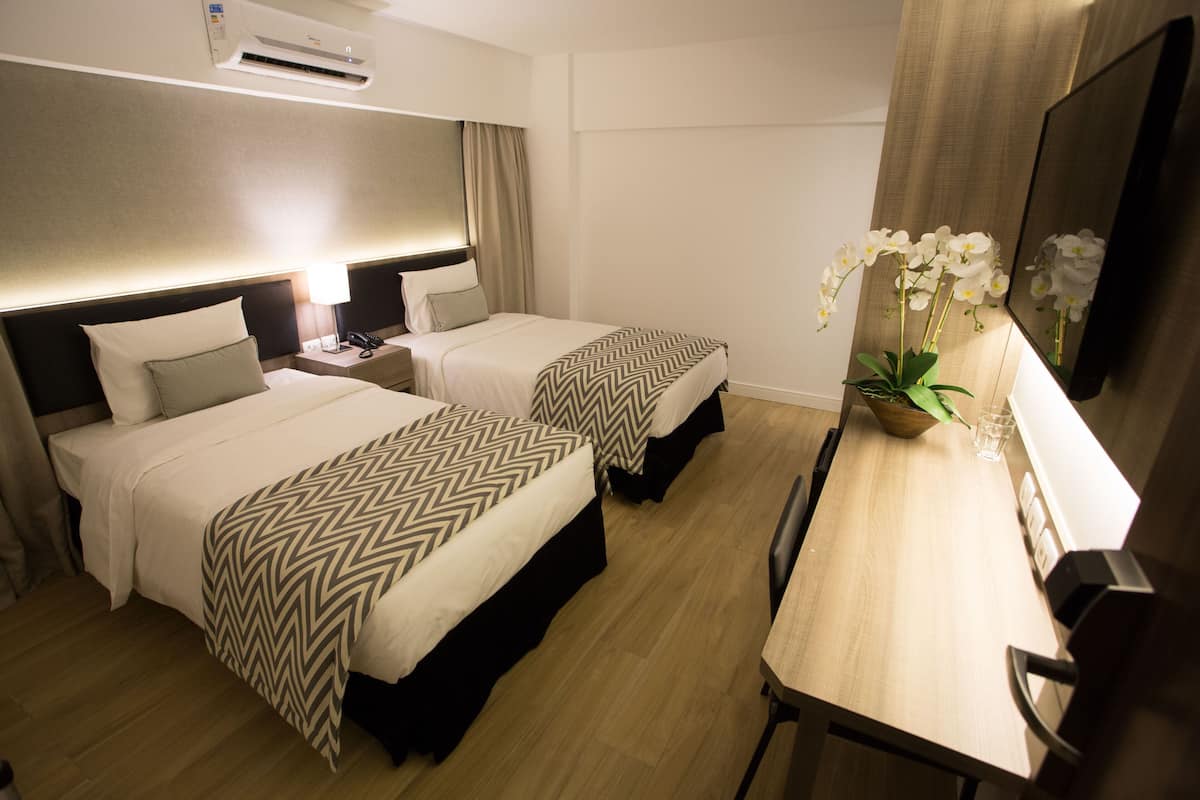 Ein Hotelzimmer mit zwei Betten, einem Schreibtisch, einem Sessel und einer Zimmerpflanze.