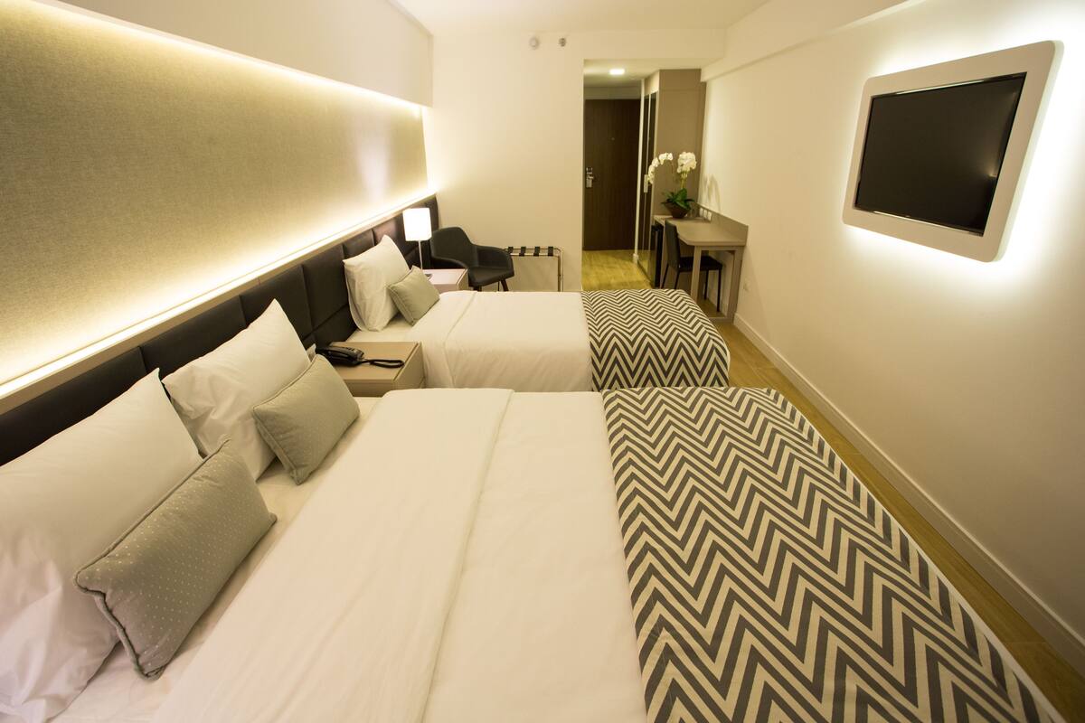 A hotel room with two beds, a desk, a chair, and a TV mounted on the wall.