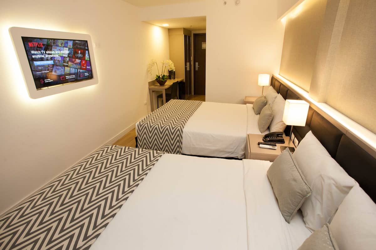 A hotel room with two beds, a desk, a TV mounted on the wall, and a bathroom visible through an open door.