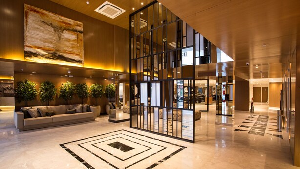 Un hall d’entrée spacieux au design moderne, agrémenté d’un grand tableau abstrait, d’un canapé d’angle et d’un motif décoratif sur le sol.