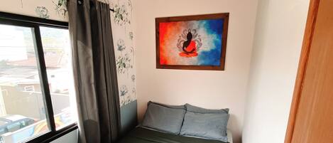 Un dormitorio pequeño con una cama, una ventana, un papel tapiz floral en la pared y un cuadro.