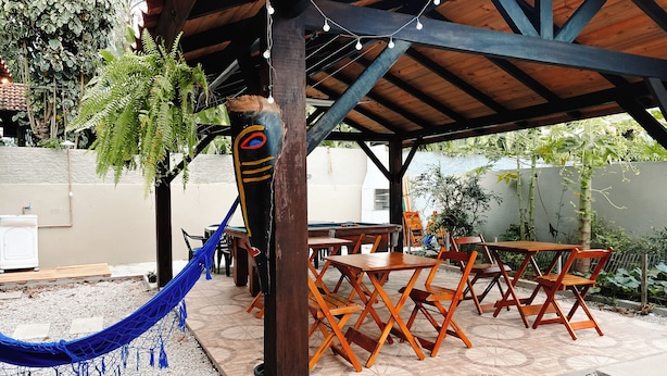 An outdoor patio with wooden tables and chairs, a hammock, and string lights. - Sagui Hostel (Florianópolis)