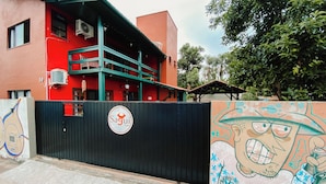 A hostel with a red exterior, a black gate with a logo, and a mural on the gate. - Sagui Hostel (Florianópolis)