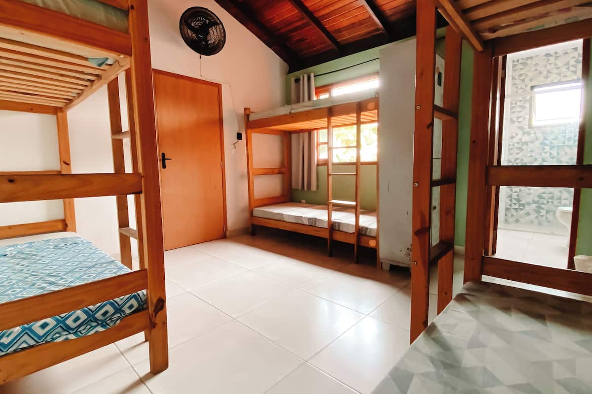 A room with two bunk beds, a wooden ceiling, a fan, and a view of the bathroom through a door.