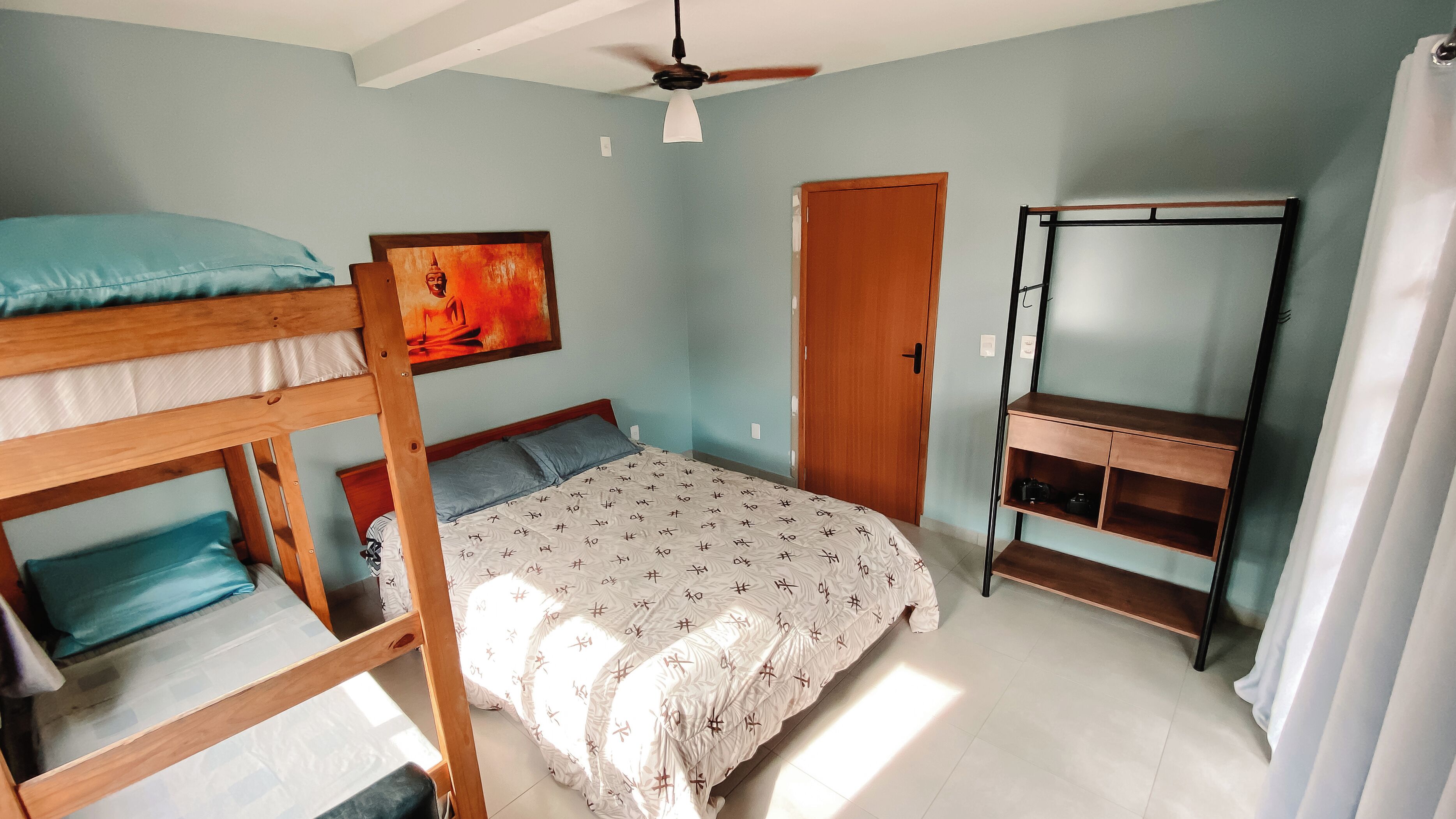 A bedroom with bunk beds, a bed with patterned bedding, a ceiling fan, a wooden wardrobe, and a shelf unit.