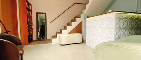 A modern living room with a staircase, a sofa, and a bookshelf.