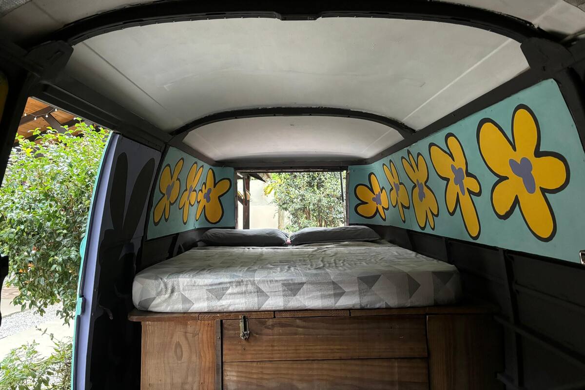 A van interior with a bed, wooden storage, and flower decals on the walls.