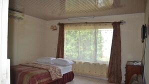 A bedroom with a bed, a window with curtains, a radiator, and a small wooden side table. - Victoria Guest House (Limbe)