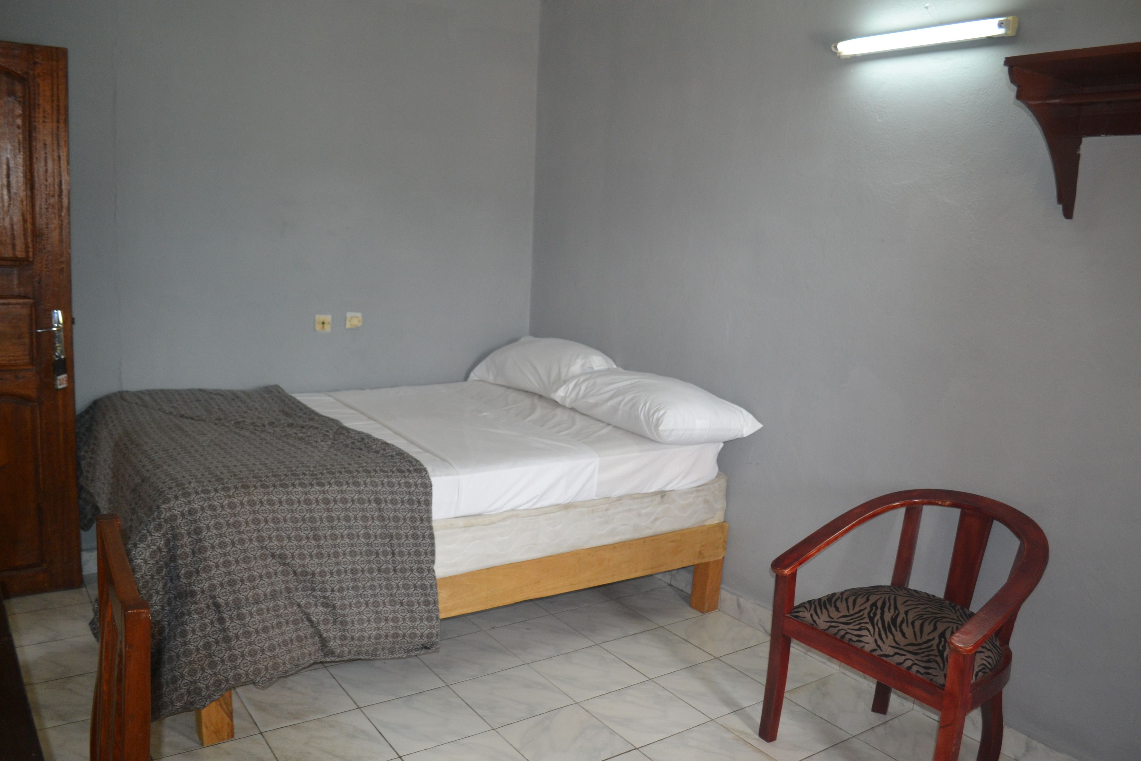 Un dormitorio con cama, una silla y un aplique de pared.