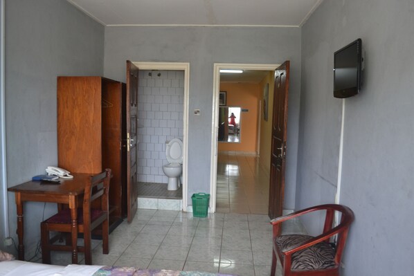 Una habitación de hotel con un escritorio de madera, una silla, una cama, televisión y un baño con inodoro y lavamanos.