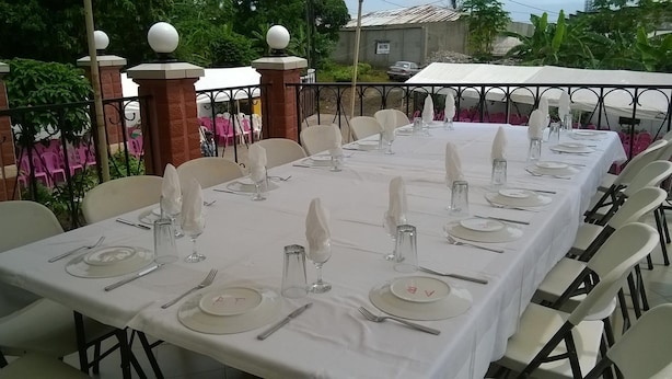 A long dining table set for a formal event with white tablecloths, plates, cutlery, and glassware. - Victoria Guest House (Limbe)