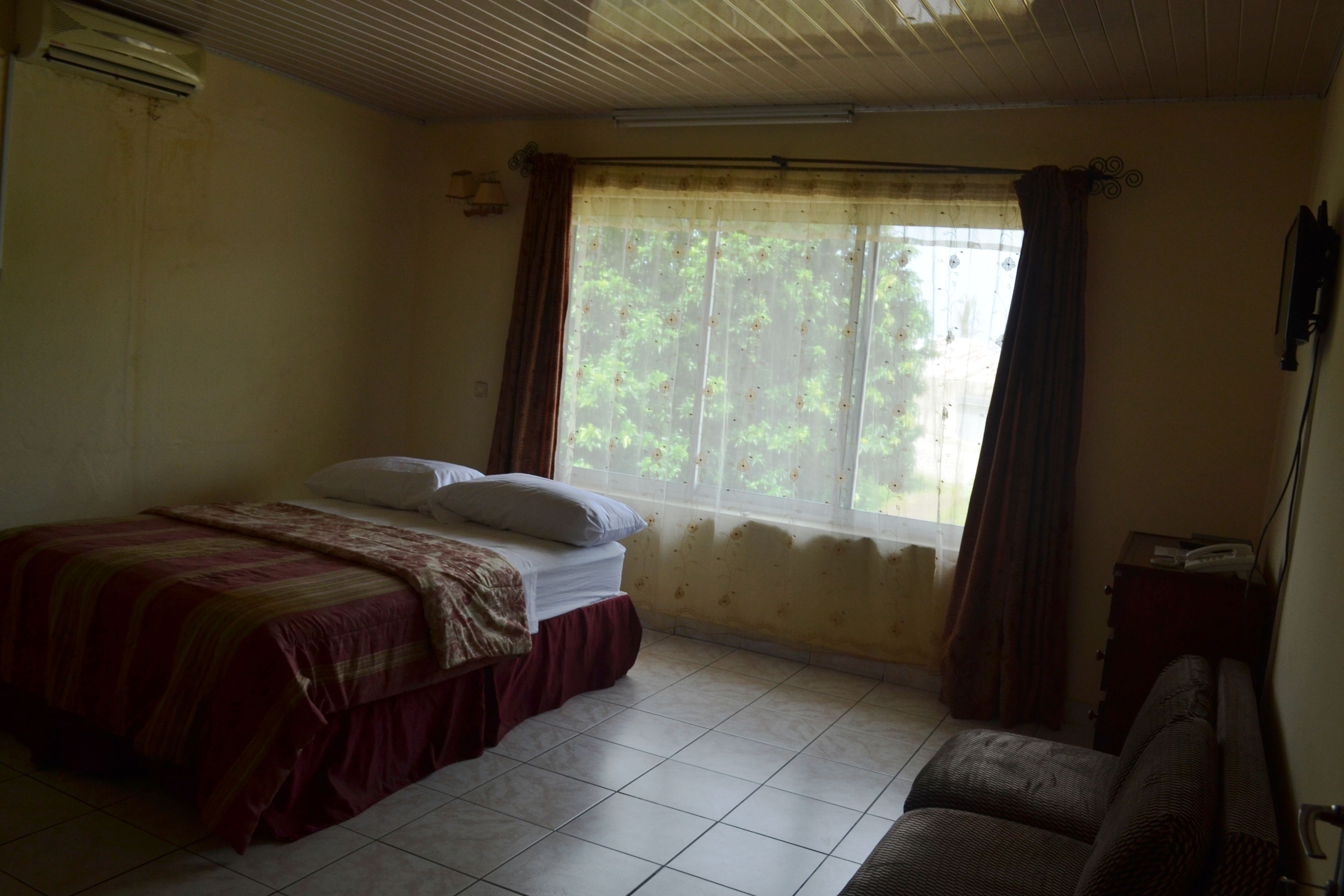 Un dormitorio con cama, sofá, ventana con cortinas y equipo de aire acondicionado.
