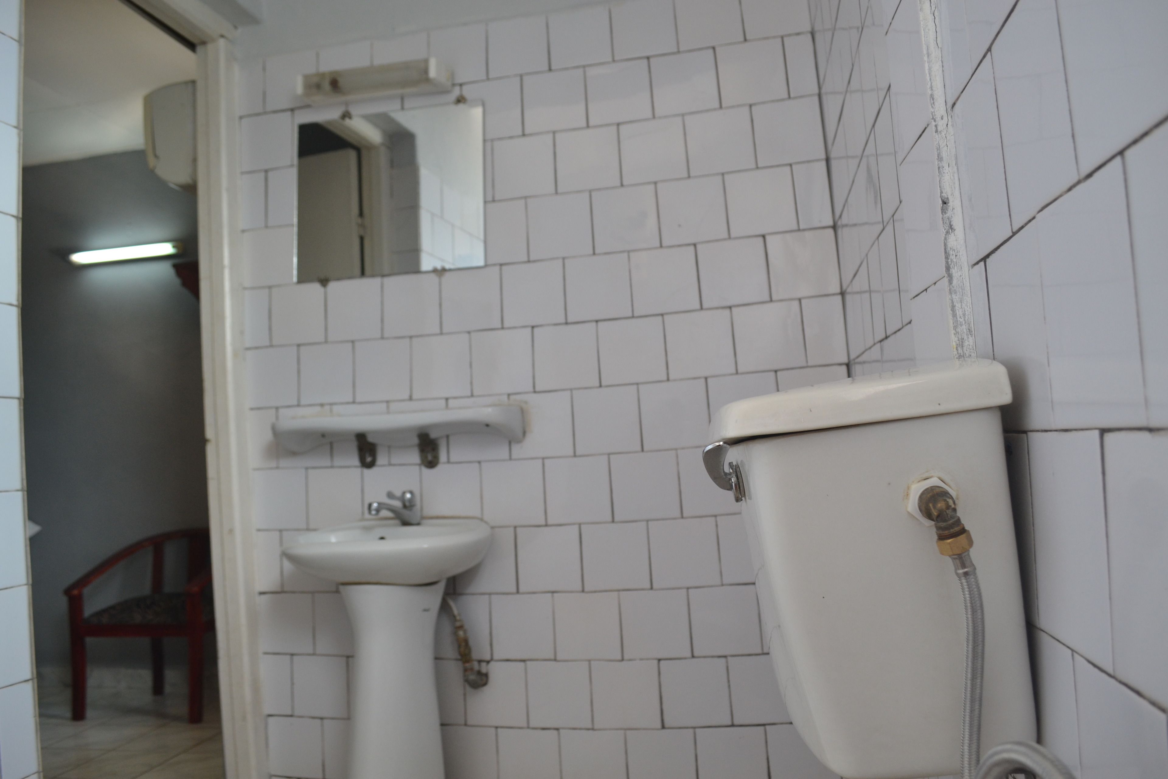 A bathroom with white tiled walls, a white sink, and a toilet.