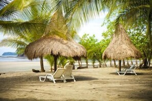Une plage avec des cabanes aux toits de chaume et des chaises longues blanches.