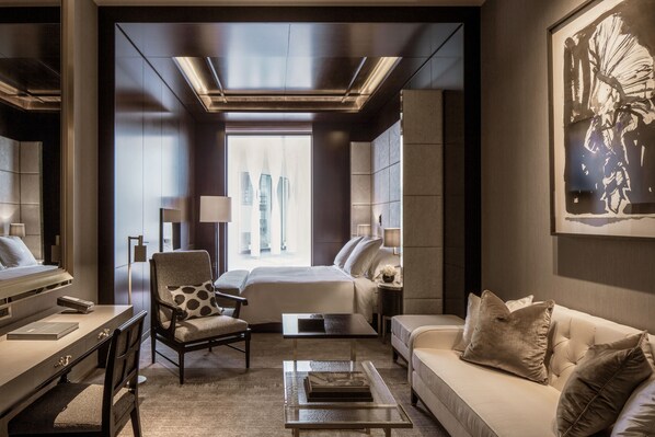 A modern hotel room with a large bed, a sitting area with a sofa and armchair, a desk, and a coffee table. - Four Seasons Hotel London at Tower Bridge (London)