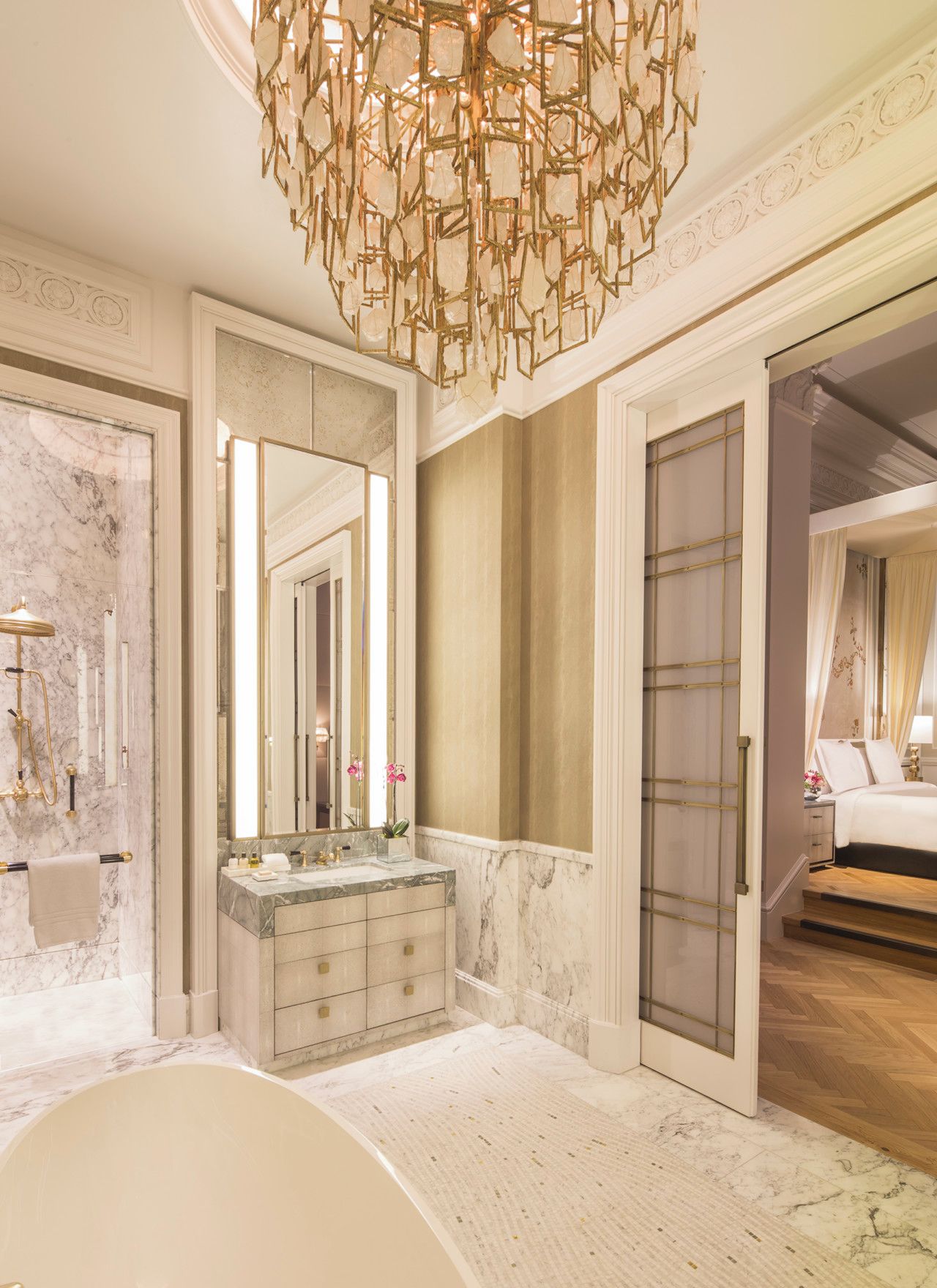 A luxurious bathroom with a marble sink, a large mirror, and a unique geometric chandelier.