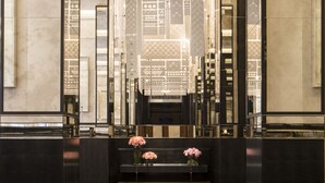 A reception area with a dark reception desk, a decorative screen with geometric patterns, and a bench with vases of flowers. - Four Seasons Hotel London at Tower Bridge (London)