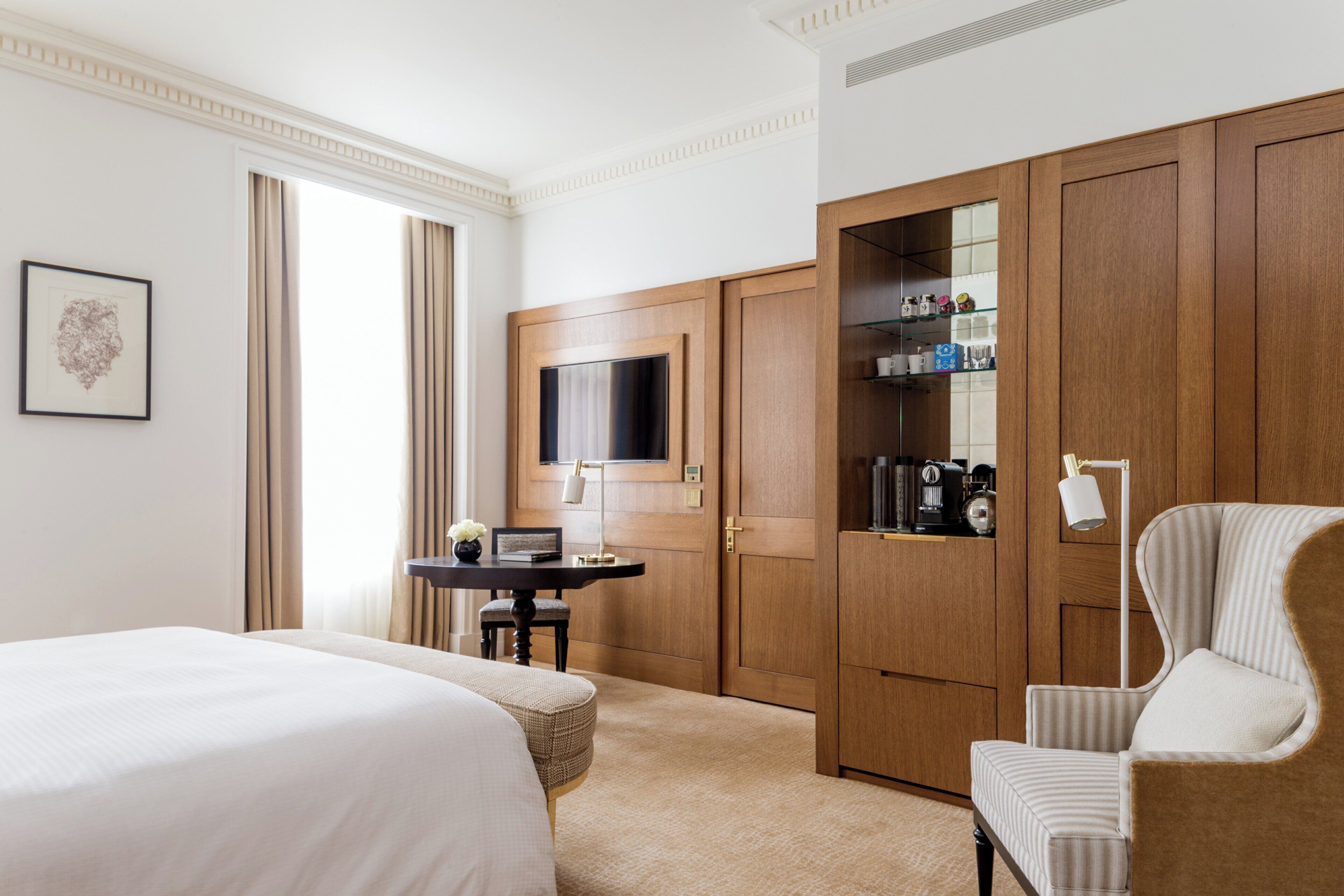 A hotel room with a large bed, a desk with a lamp, a wardrobe, and a television.