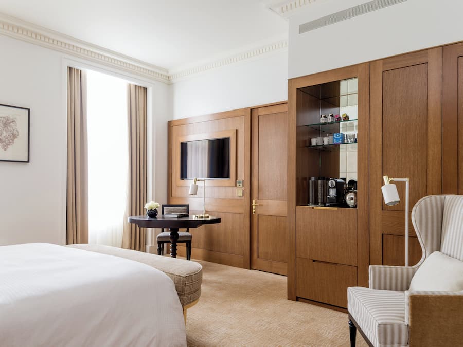 A hotel room with a large bed, a desk with a lamp, a wardrobe, and a television.
