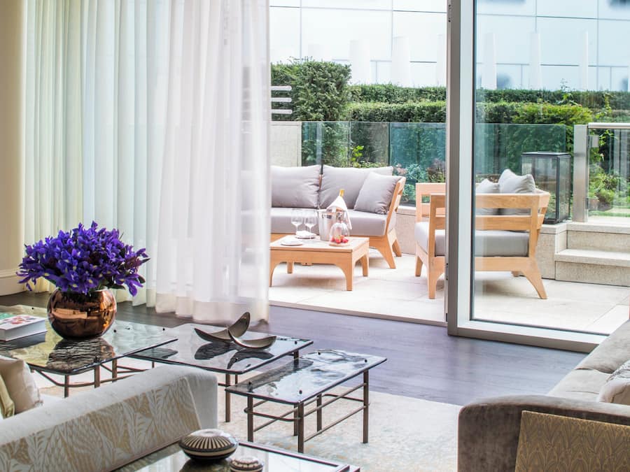 Una sala de estar moderna con un ventanal que da a un balcón con mobiliario exterior.