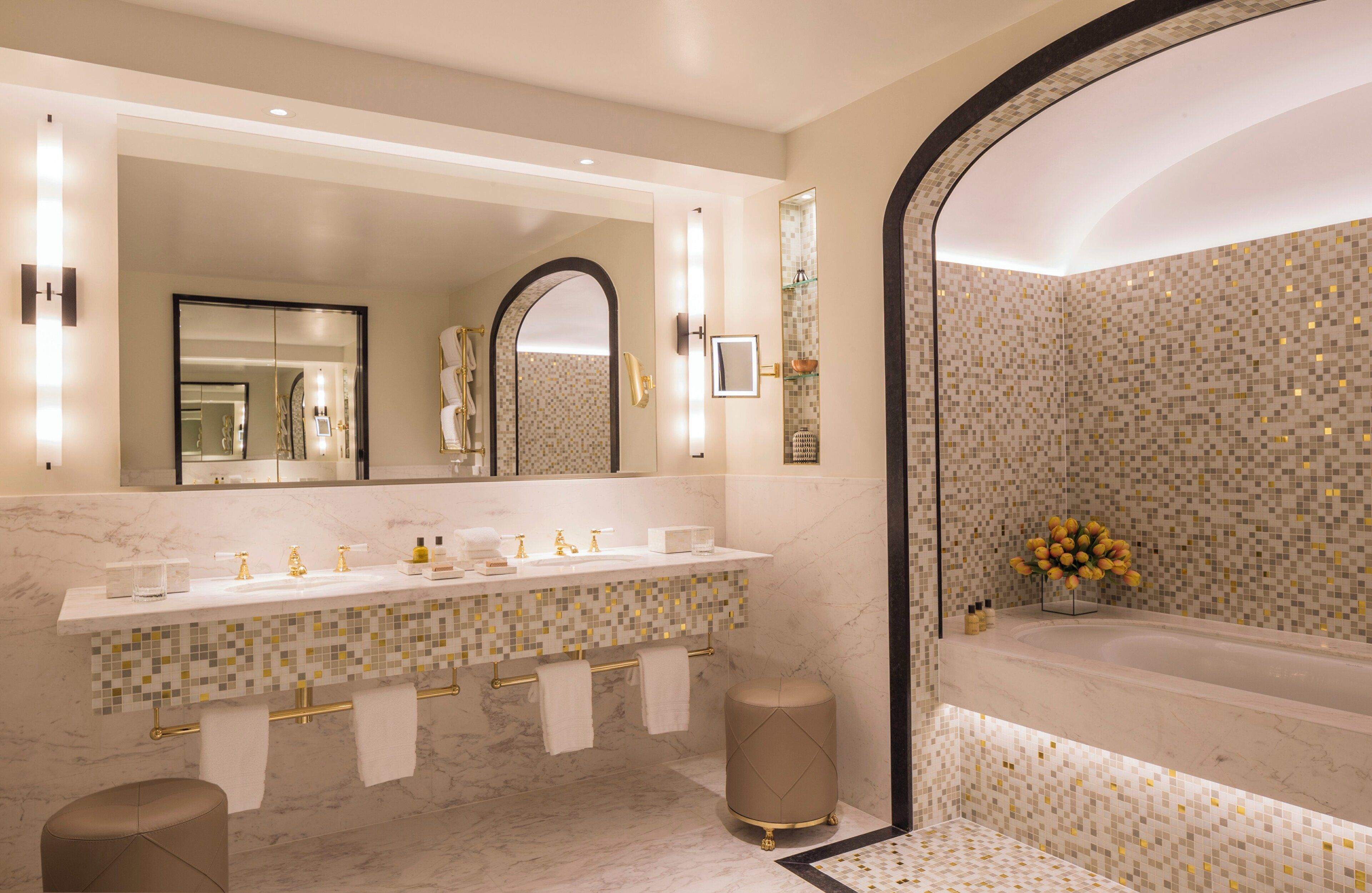 A modern bathroom with a large mirror, a vanity with a tiled backsplash, and a bathtub.