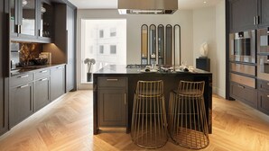 A modern kitchen with dark cabinetry, a central island with stools, and a large window providing natural light. - Four Seasons Hotel London at Tower Bridge (London)