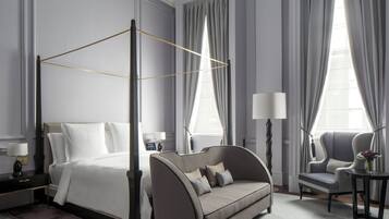 Una habitación de hotel moderna con una cama con dosel, un sofá, una silla y una mesita con un florero.
