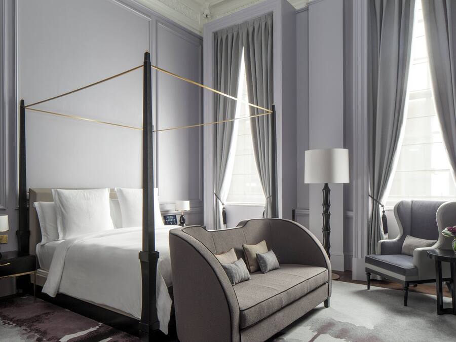 Una habitación de hotel moderna con una cama con dosel, un sofá, una silla y una mesita con un florero.