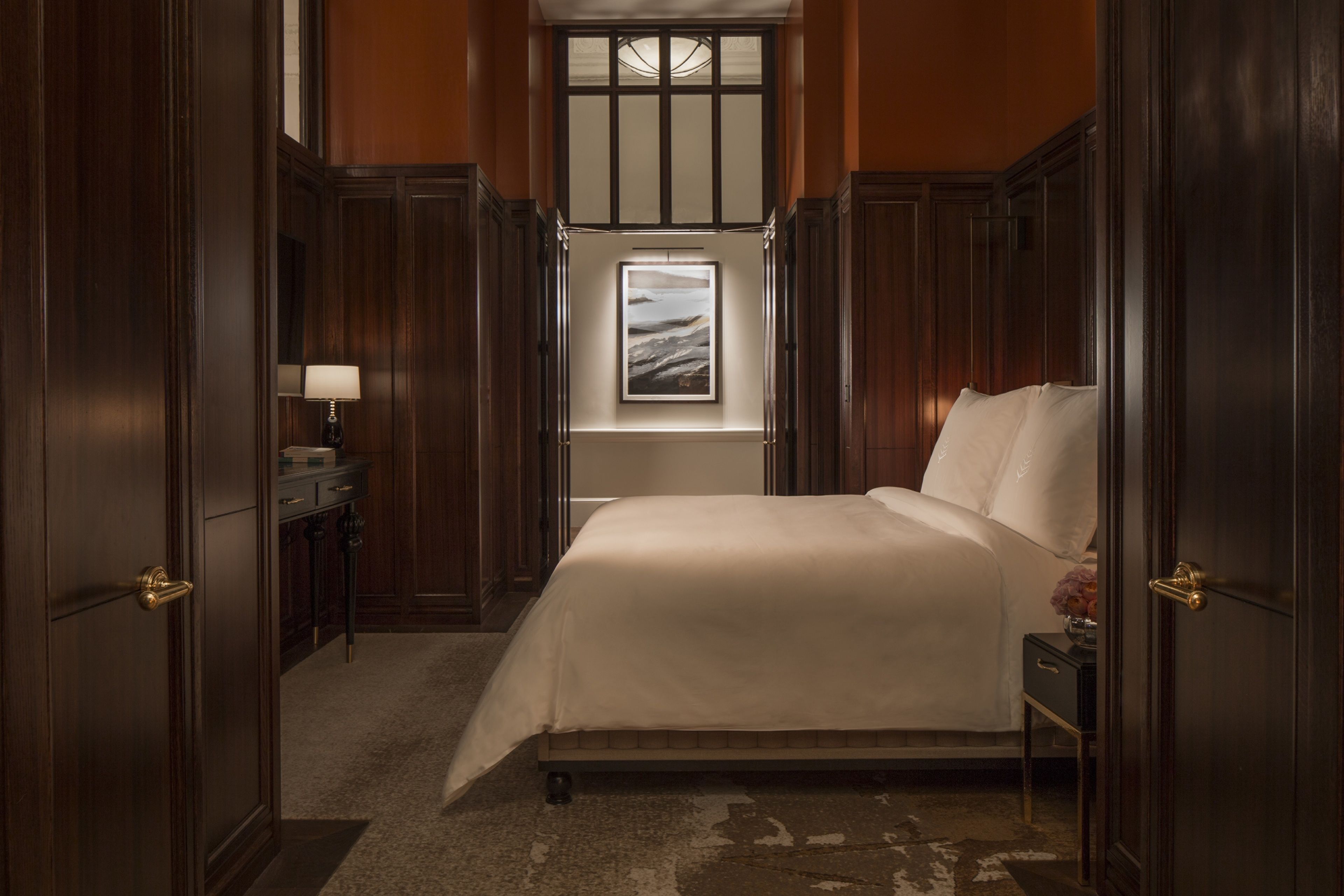 Une chambre d’hôtel avec un grand lit, une table de chevet, une lampe, une fenêtre donnant sur un beau paysage et un lambris en bois.