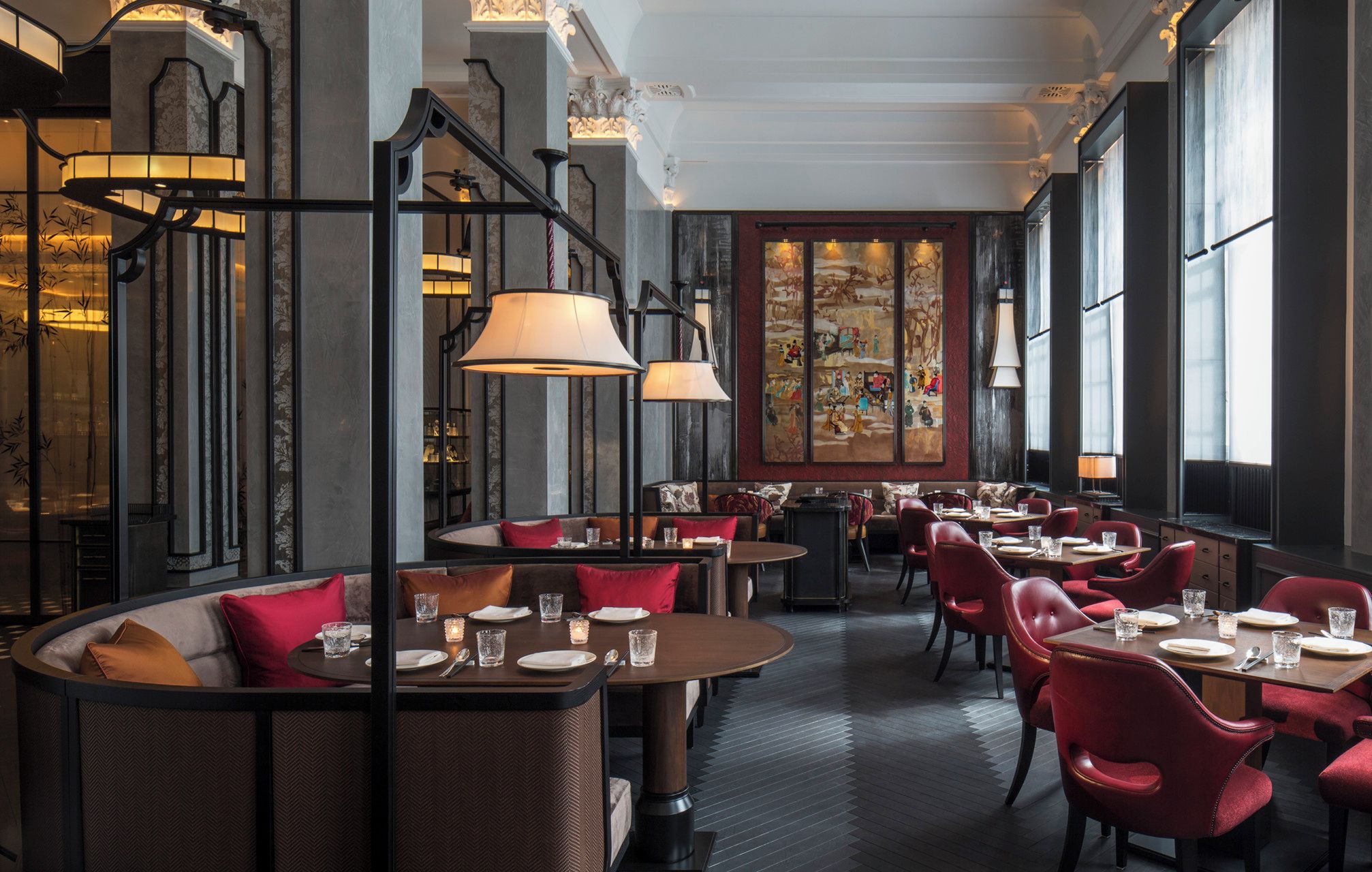 Ein Restaurant mit runden Tischen, rot gepolsterten Stühlen und einem großen Wandgemälde.