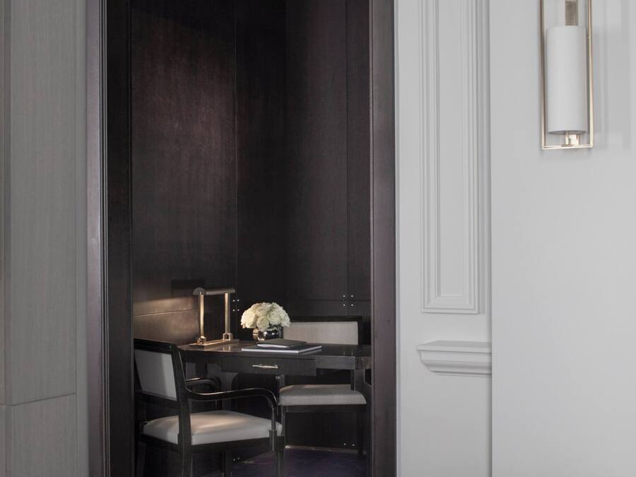 Una camera moderna con pavimento in legno scuro, un letto bianco, una scrivania con sedia, un vaso con fiori e un lampadario.