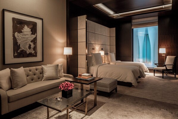A hotel room with a sofa, two beds, a coffee table with a vase, and a large window with curtains. - Four Seasons Hotel London at Tower Bridge (London)