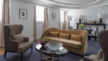 Un salon moderne avec un canapé beige, une table basse en verre et deux fauteuils. On aperçoit à l’arrière-plan un coin repas avec une table et des chaises.