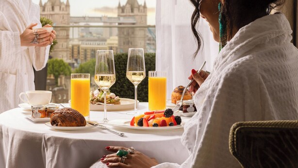 A breakfast setting with a croissant, fruit, and juice on a table, with a city view in the background. - Four Seasons Hotel London at Tower Bridge (London)