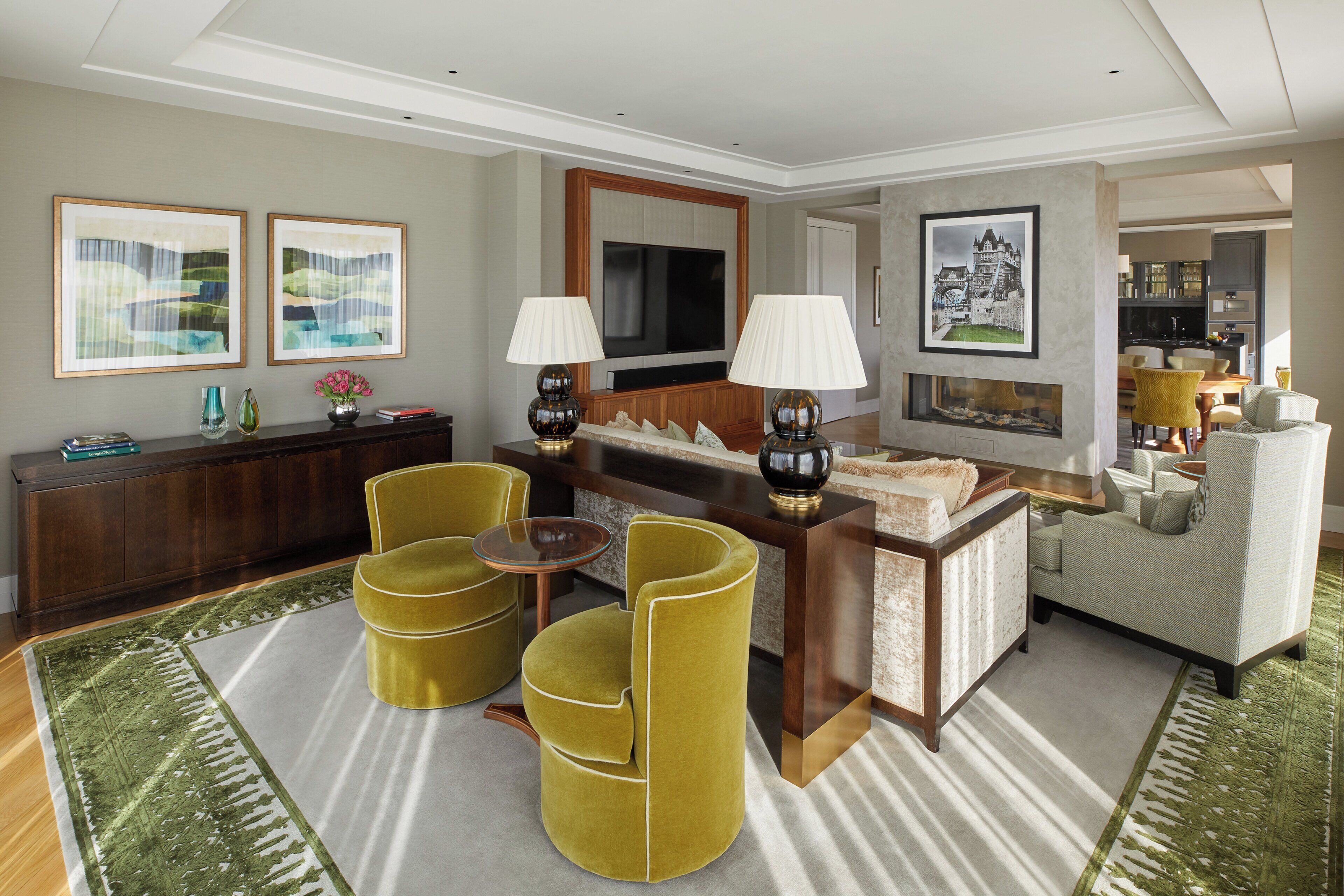 A modern living room with a sofa, two armchairs, a coffee table, and a TV. There are framed pictures on the walls and a decorative vase on the side table.