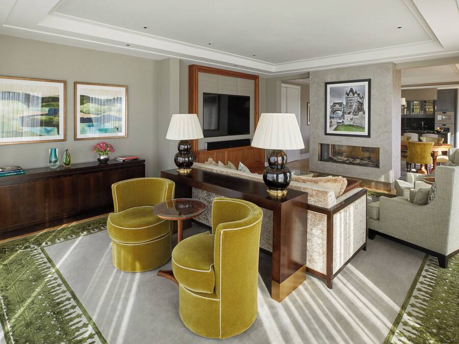 A modern living room with a sofa, two armchairs, a coffee table, and a TV. There are framed pictures on the walls and a decorative vase on the side table.