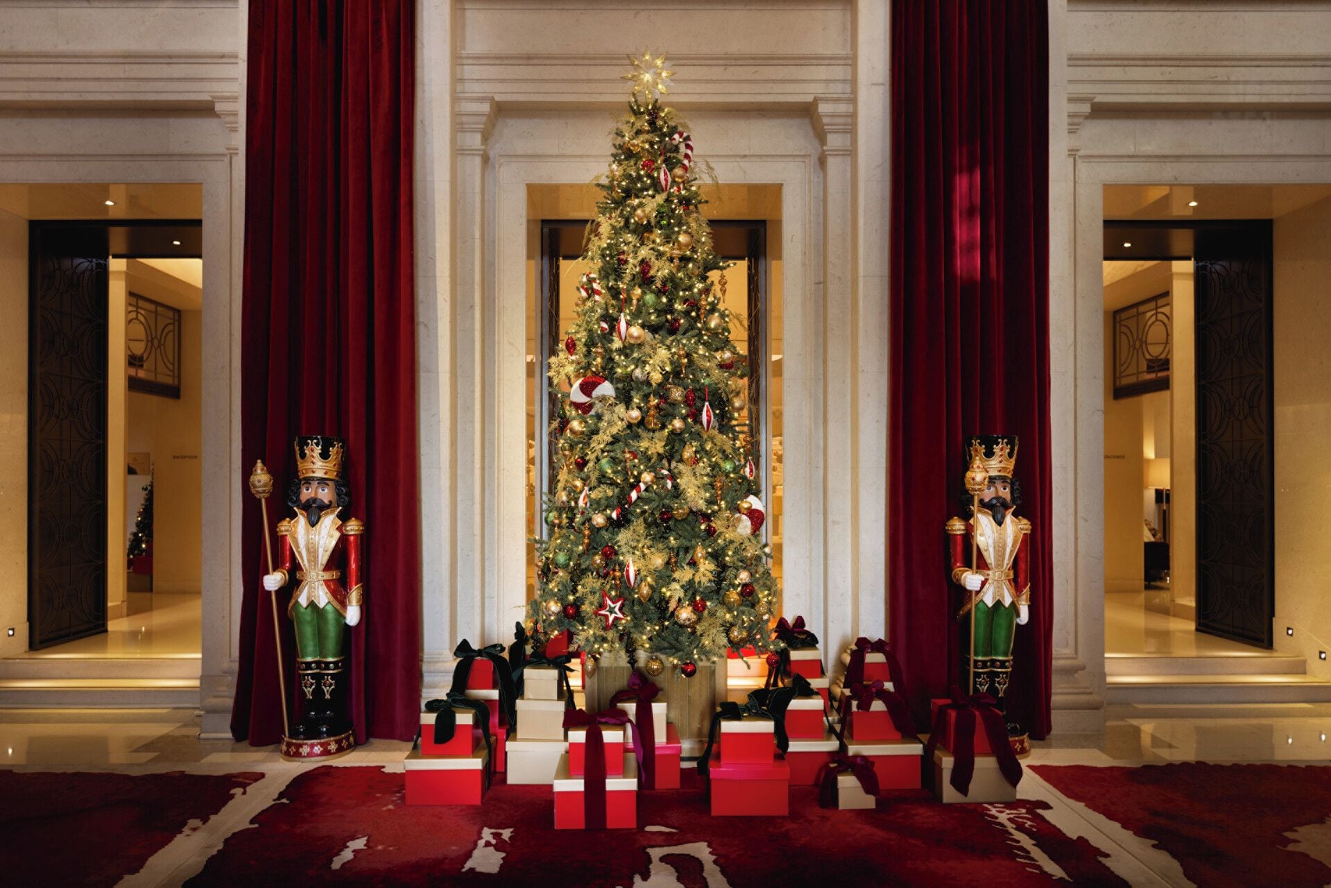 Un vestíbulo elegante con un gran árbol de Navidad, cortinas rojas y dos ornamentadas estatuas de rompecabezas.