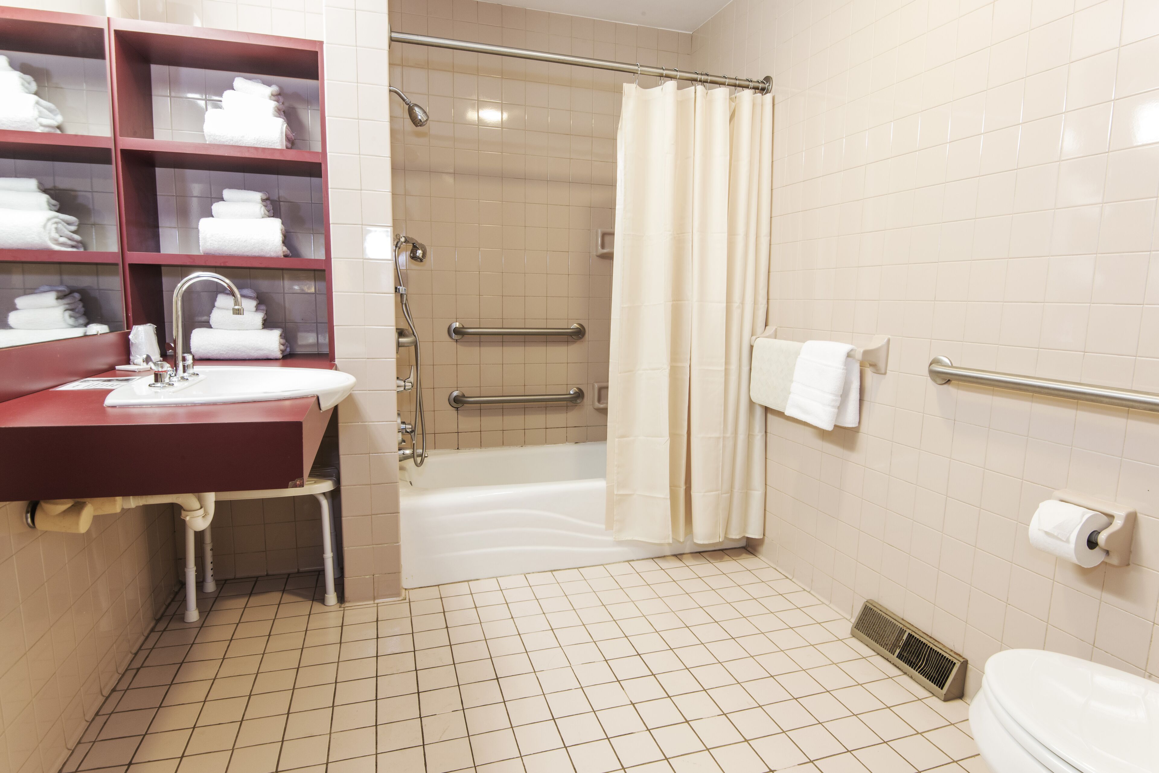 A bathroom with a sink, mirror, shelves with towels, a shower, and a toilet.