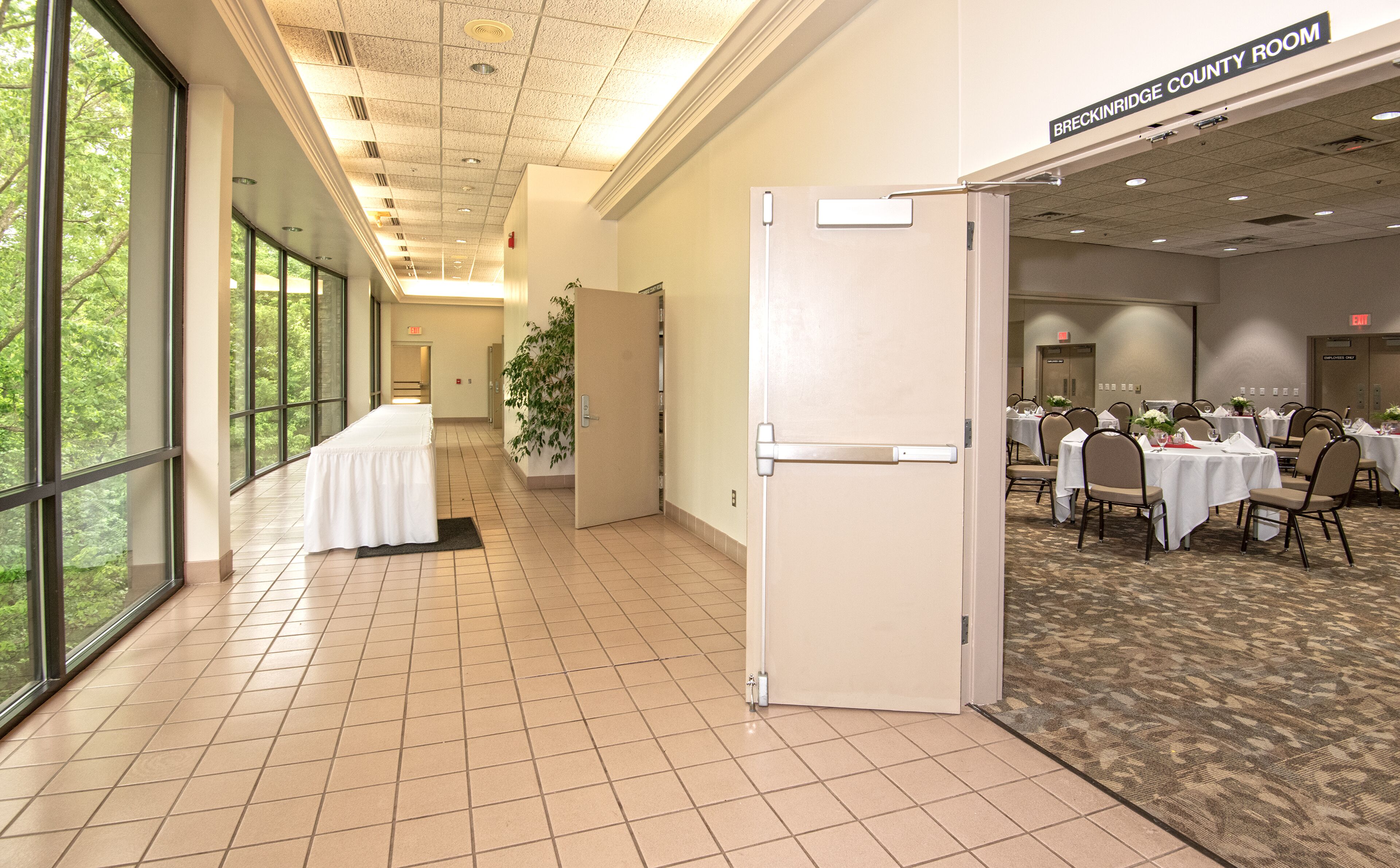 A conference room with a long table, a door leading to another room, and a carpeted area with tables and chairs.