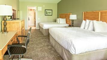 A hotel room with two beds, a desk, a chair, and a lamp.