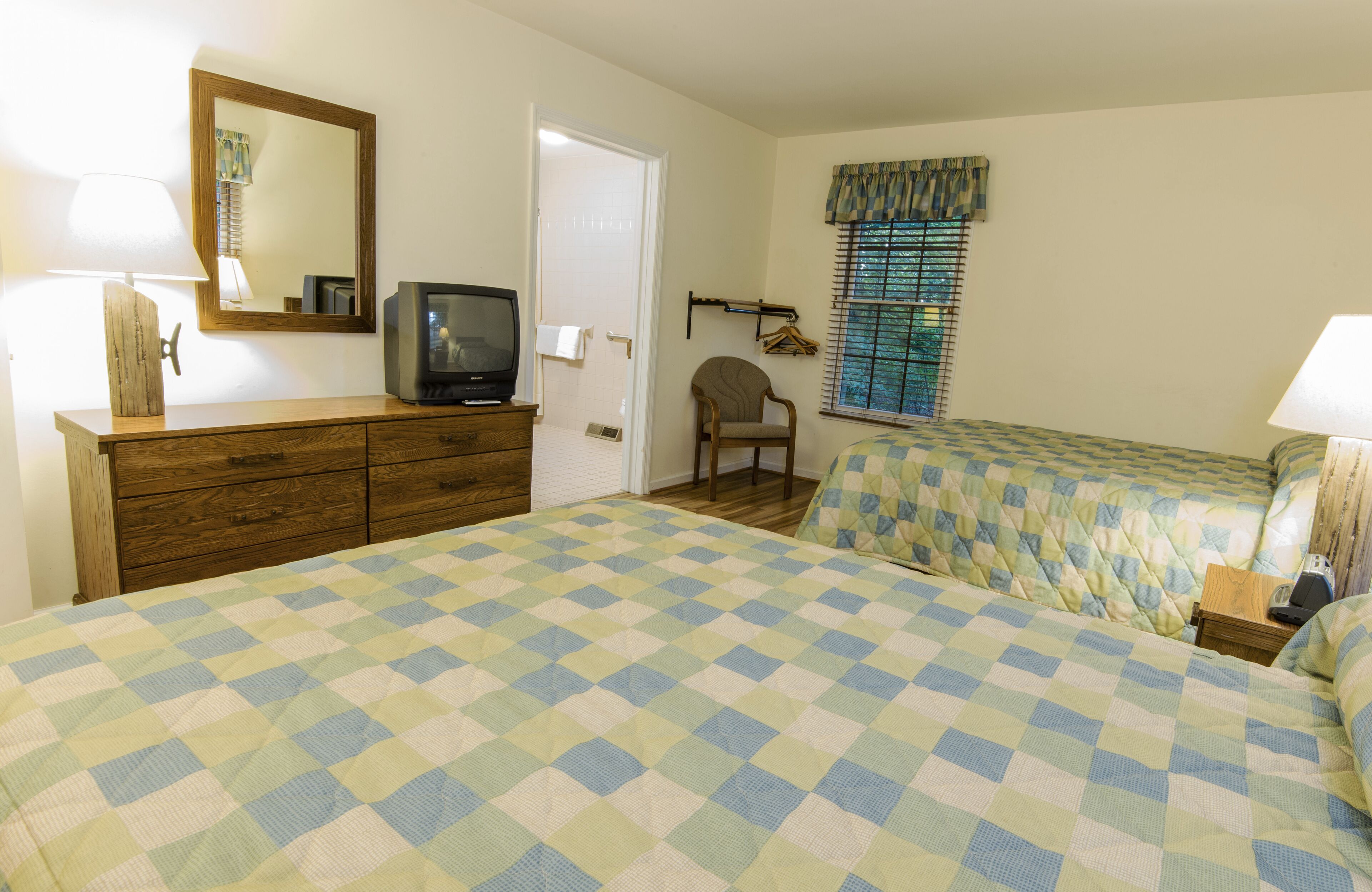 A bedroom with two beds, a dresser, a television, and a chair.